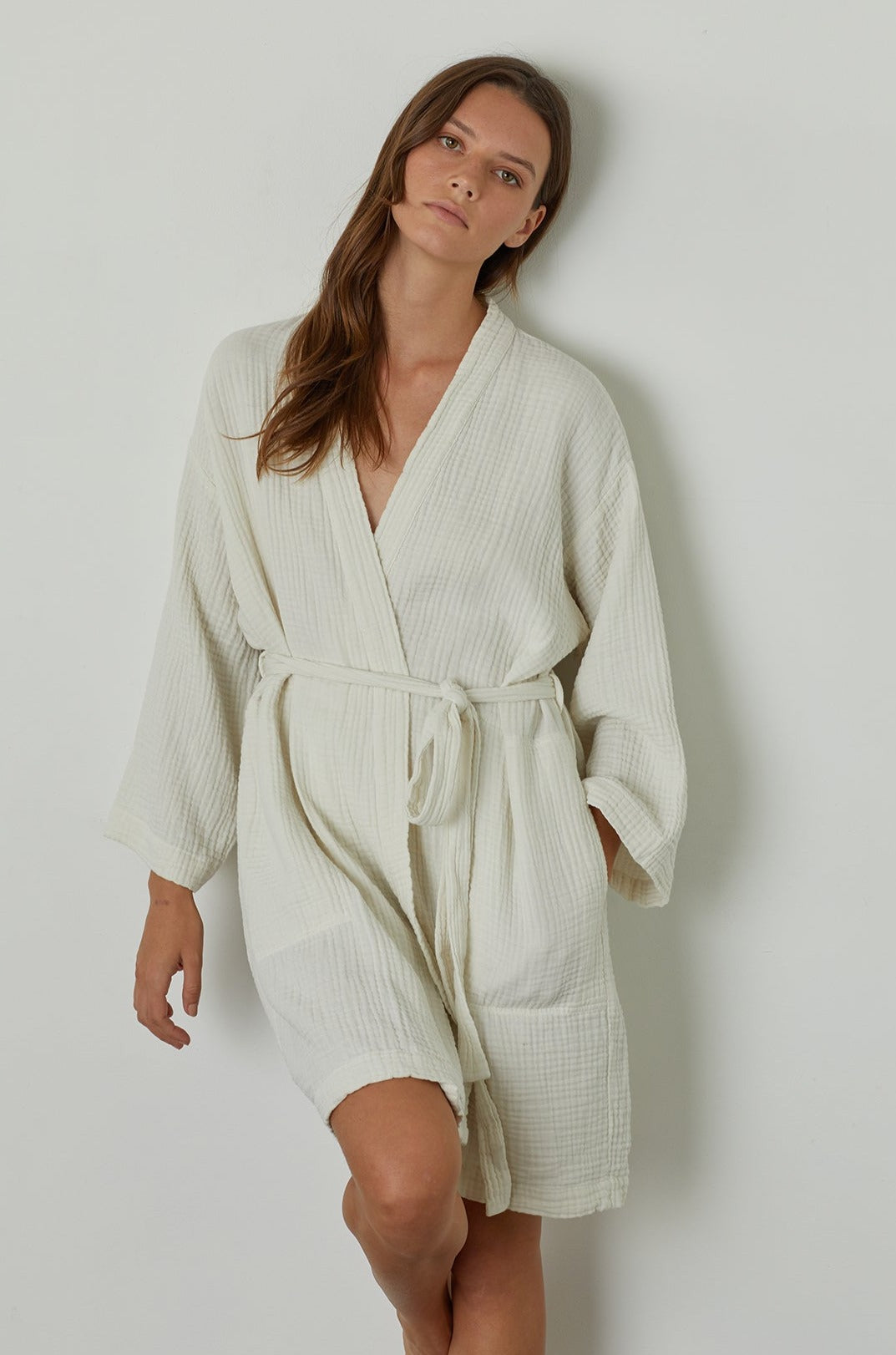   A woman wearing a MINI COTTON GAUZE ROBE by Jenny Graham Home standing against a wall. 