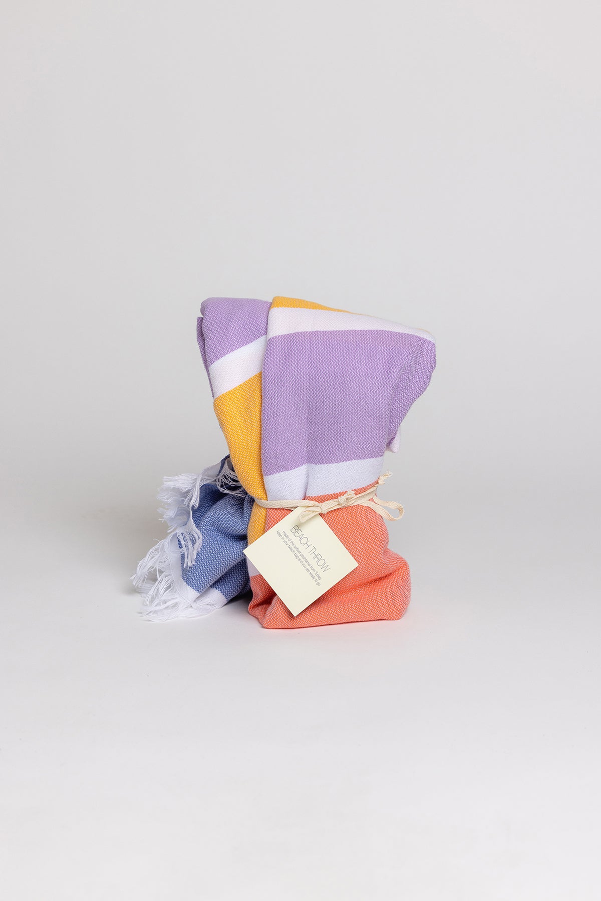   A purple, yellow, and orange striped Velvet by Graham & Spencer beach throw on a white background. 