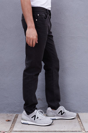 a man wearing Joseph Cotton Canvas Pant by Velvet by Graham & Spencer and sneakers standing next to a gray wall.
