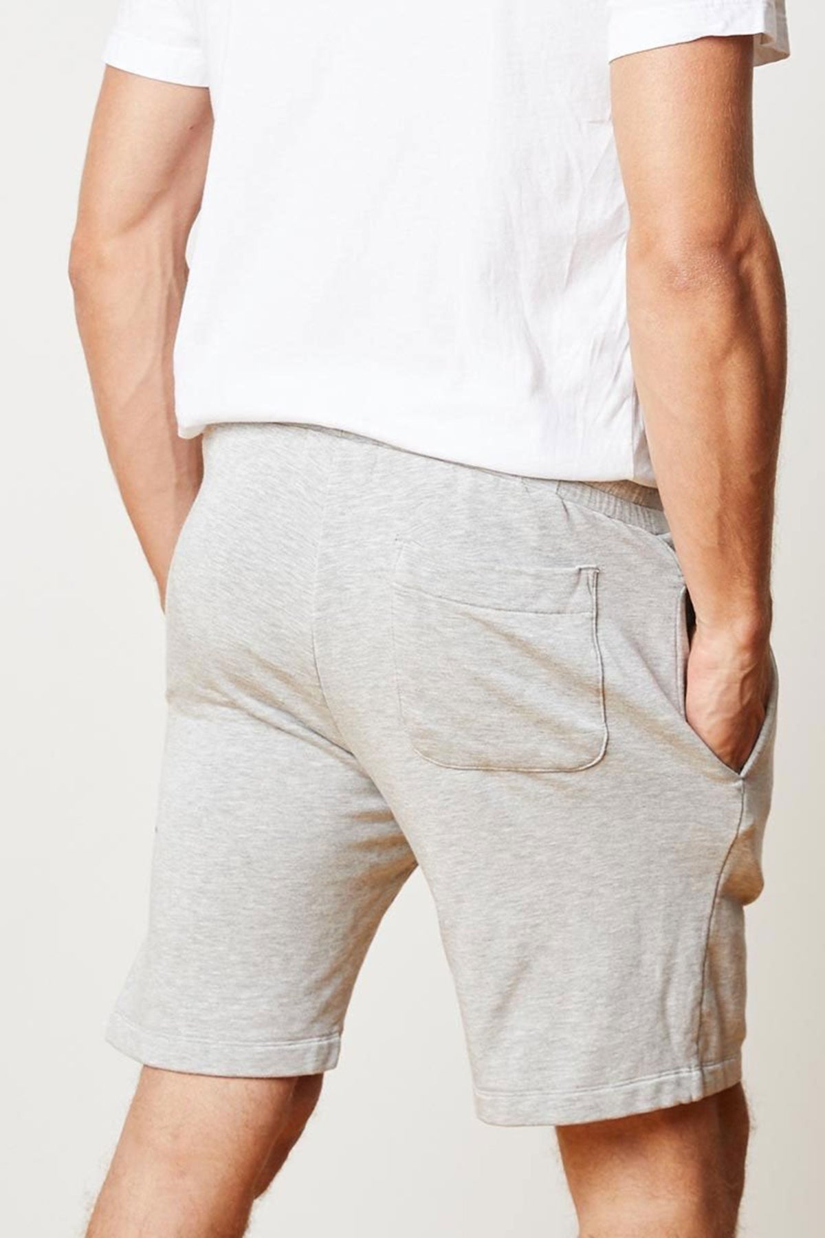   A person wearing a white t-shirt and gray ATLAS LUXE FLEECE DRAWSTRING SHORT by Velvet by Graham & Spencer with hands in pockets, viewed from behind. 