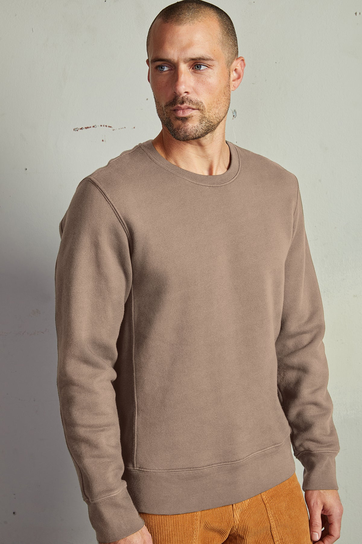   A man in a Velvet by Graham & Spencer King Crew Neck Sweatshirt and brown pants with clean lines, perfect for everyday minimal style. 