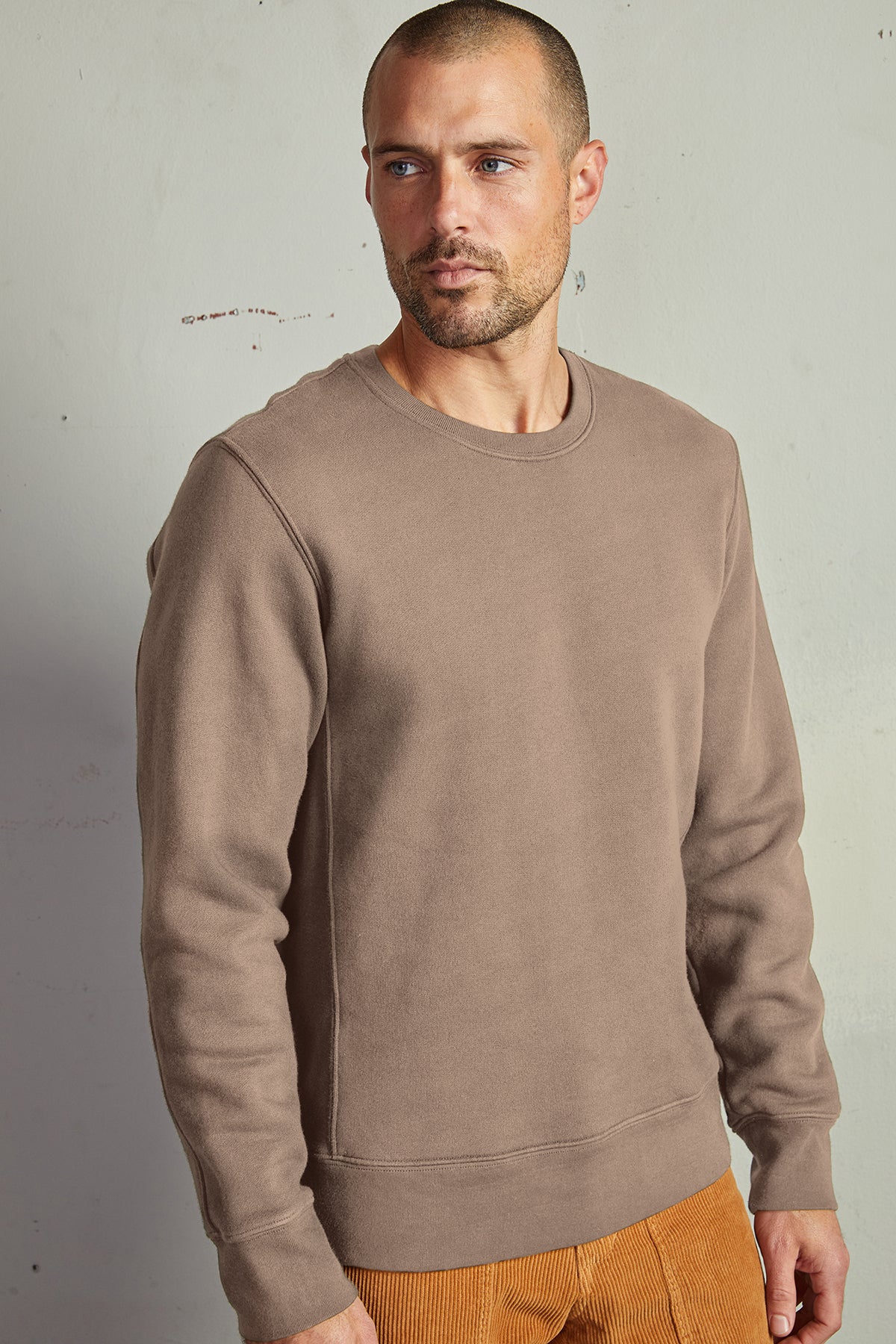 A man in a Velvet by Graham & Spencer King Crew Neck Sweatshirt and brown pants with clean lines, perfect for everyday minimal style.-14904539611329
