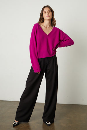 Model standing with hand on hip wearing Amika Cashmere V-Neck Sweater in bright magenta pink with Leona pant full length front with black heels