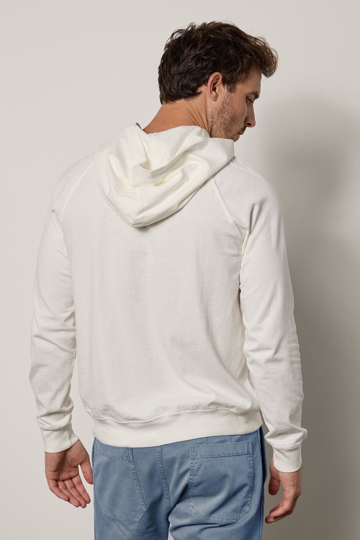   The back of a man wearing a GREG HOODIE by Velvet by Graham & Spencer and blue pants with a casual slouch. 