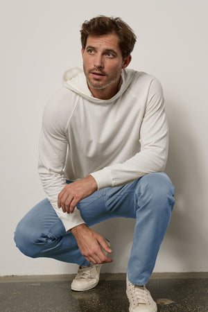 A man in a GREG HOODIE by Velvet by Graham & Spencer casually slouching against a wall.