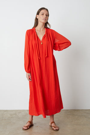 Carmella Maxi Dress in bright red cardinal color gauze model with one hand on hip facing front with gold necklace full length front