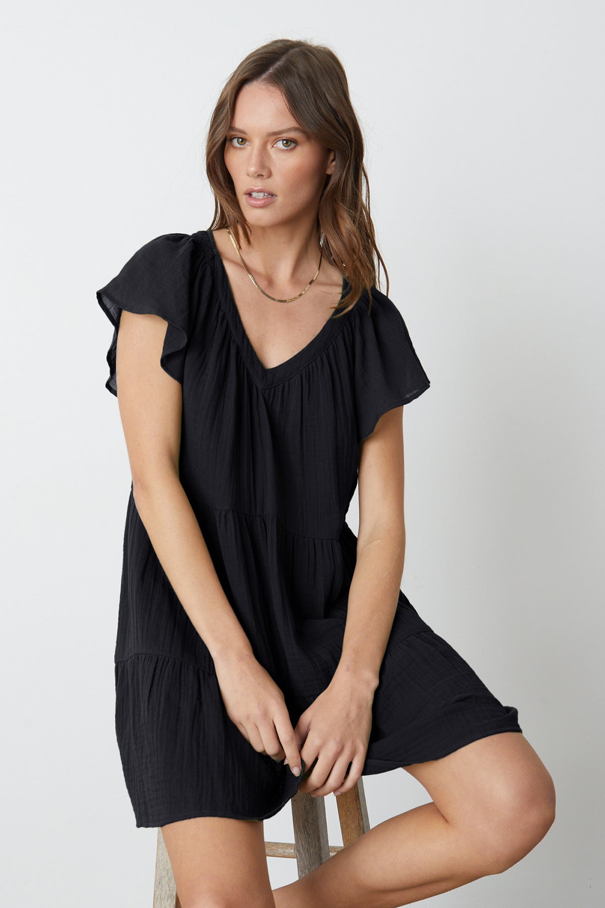Woman sitting on wooden stool wearing Eleanor Tiered Dress in black cotton gauze front-26262137274561