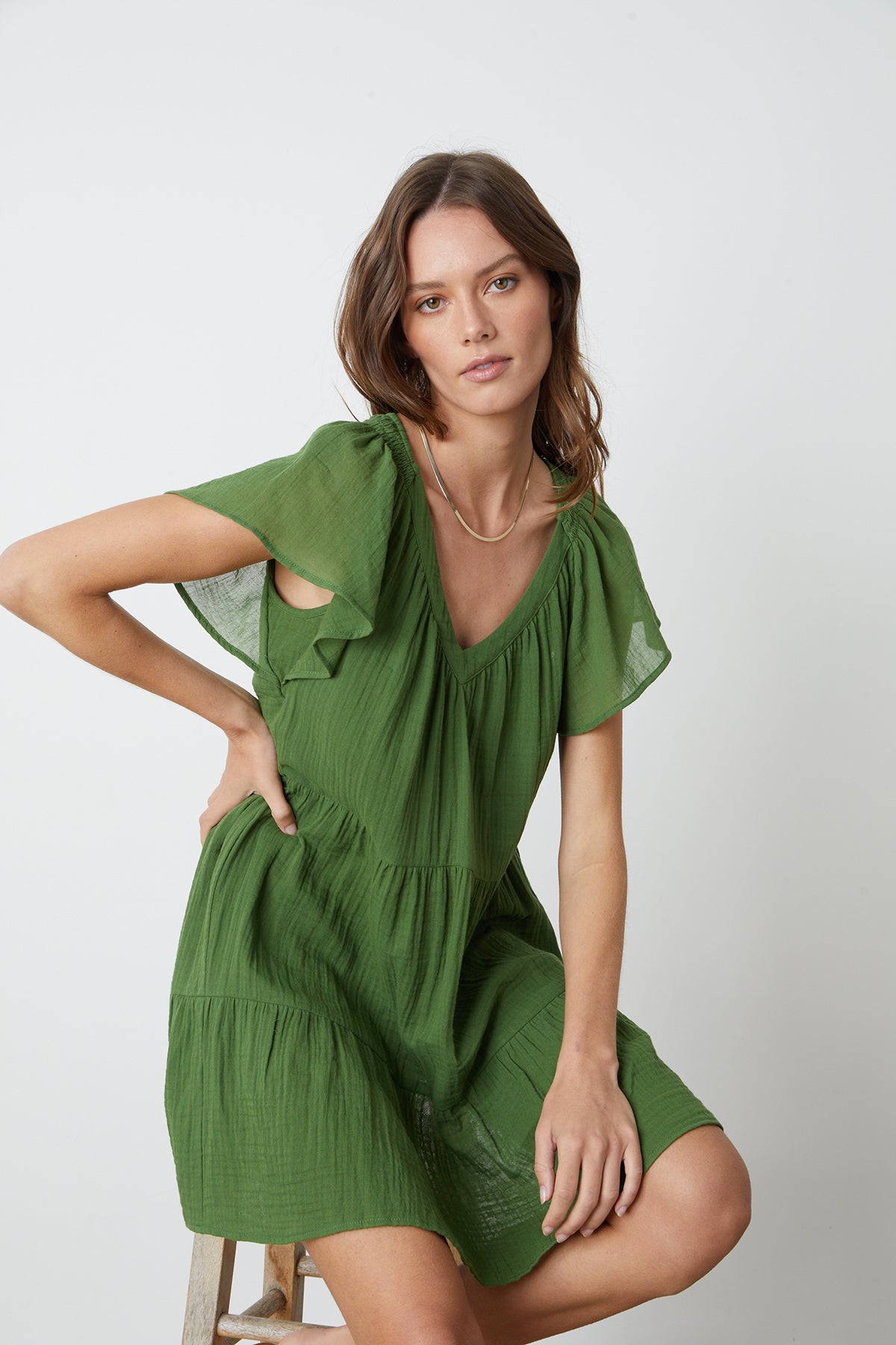 Woman sitting on wooden stool wearing Eleanor Tiered Dress in garden green cotton gauze front-26262138093761