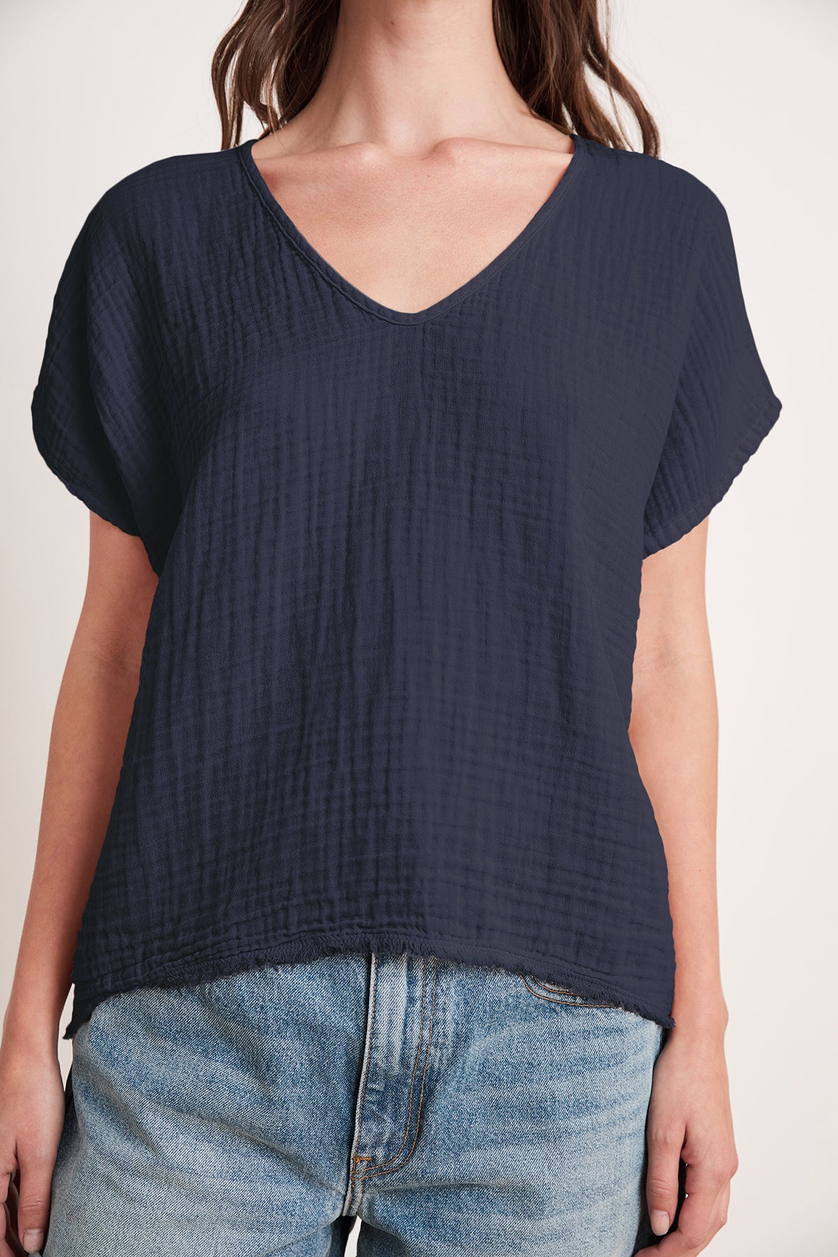   A person is wearing a relaxed fit, short-sleeved ELSA COTTON GAUZE TOP by Velvet by Graham & Spencer in navy blue, paired with light blue jeans featuring raw hem detail. 