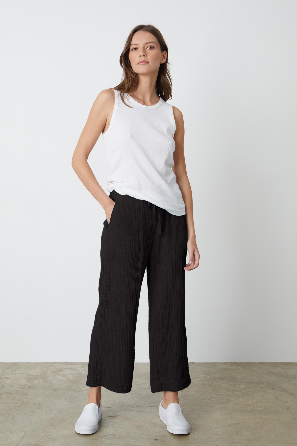 A woman wearing a white tank top and Velvet by Graham & Spencer FRANNY COTTON GAUZE PANT in black with white sneakers full length front-26262343745729