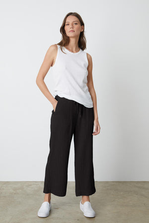 A woman wearing a white tank top and Velvet by Graham & Spencer FRANNY COTTON GAUZE PANT in black with white sneakers full length front