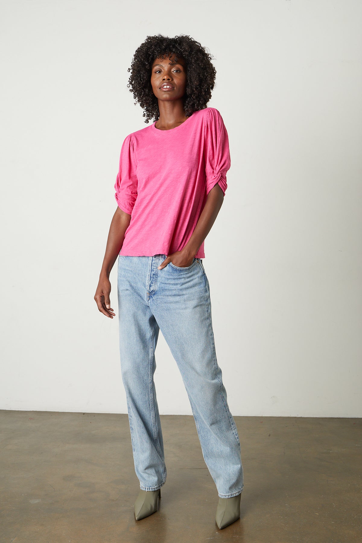   a black woman wearing a pink AMELIA PUFF SLEEVE TEE by Velvet by Graham & Spencer and jeans. 