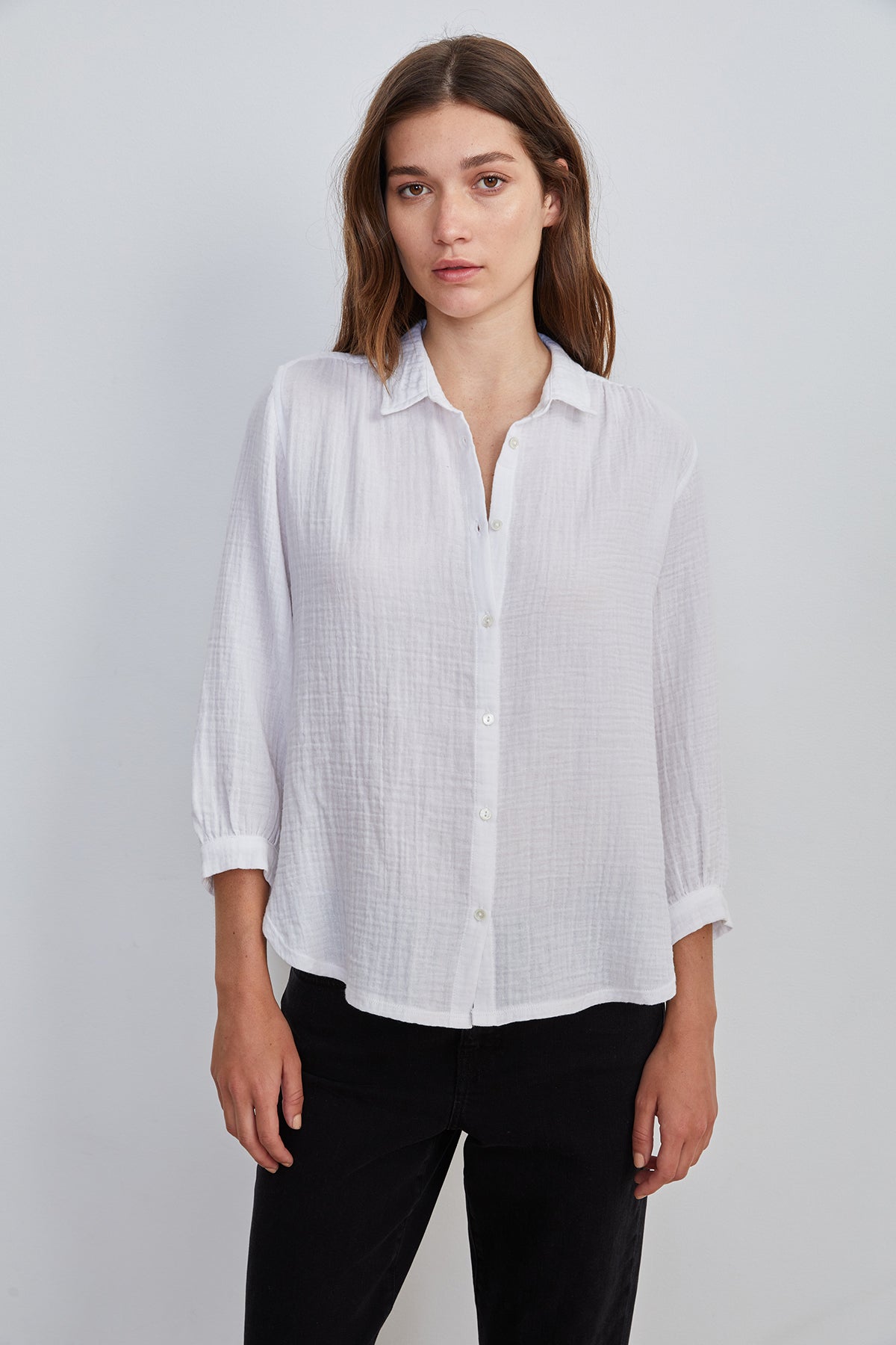   A person with long brown hair is wearing the DAYNA 3/4 SLEEVE BUTTON-UP BLOUSE from Velvet by Graham & Spencer, made from lightweight cotton slub, with the sleeves rolled up and black pants, standing against a plain white background. 