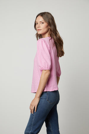 The model is wearing a Velvet by Graham & Spencer pink Joella puff sleeve tee and jeans.