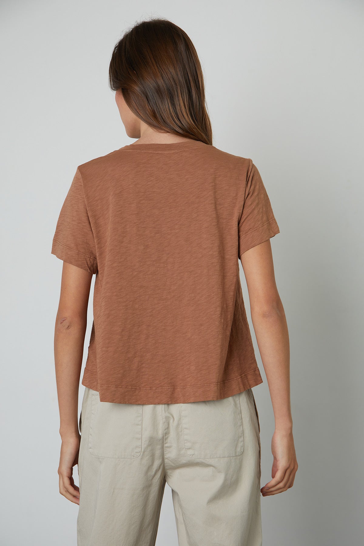 The back view of a woman wearing a Velvet by Graham & Spencer LULA COTTON SLUB SWING TEE and tan pants.-25796751032513