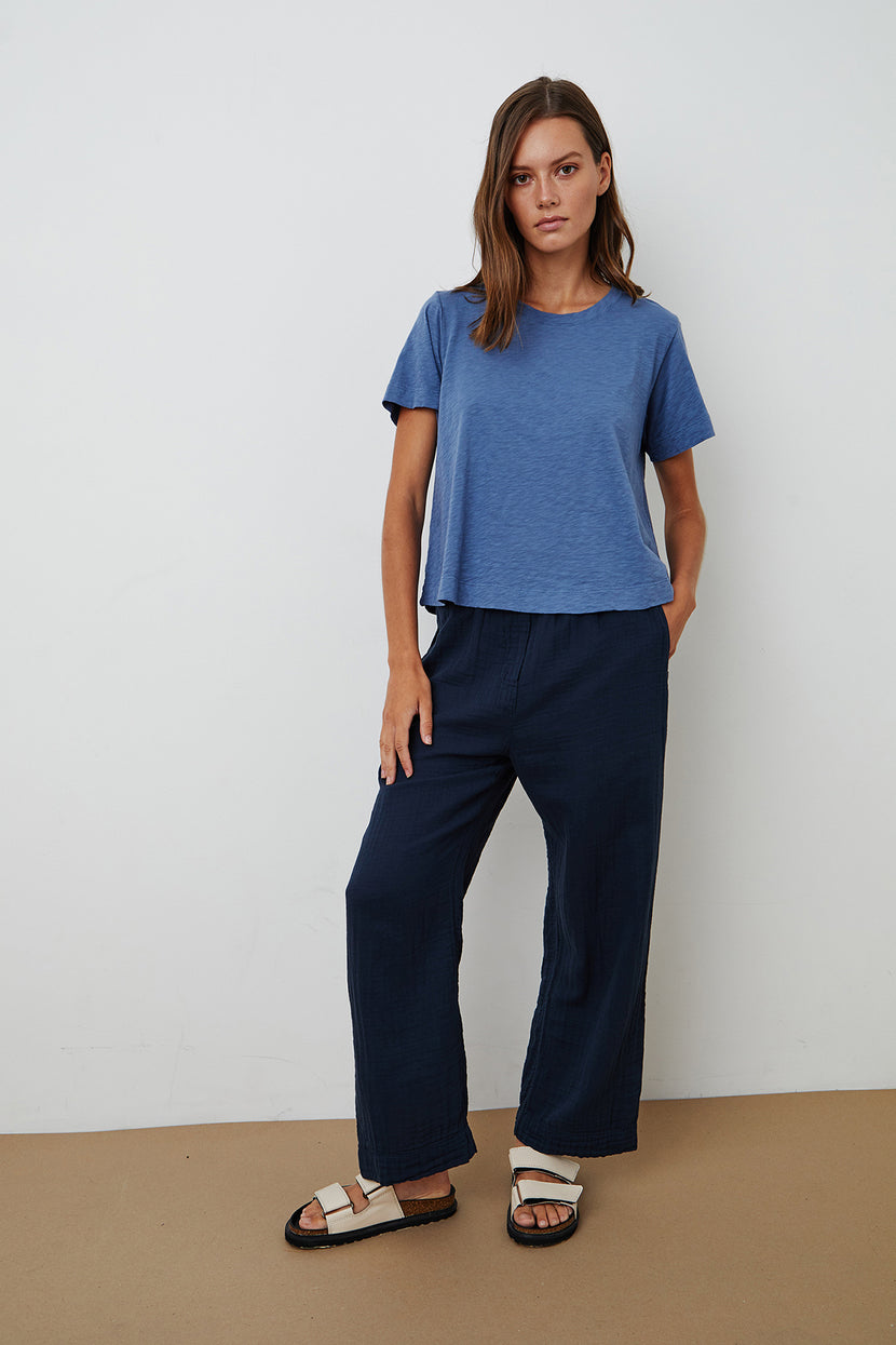 The model is wearing a blue LULA COTTON SLUB SWING TEE by Velvet by Graham & Spencer and wide leg pants.