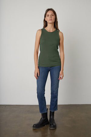 A person stands against a plain background, wearing a Velvet by Graham & Spencer MAXIE RIBBED TANK TOP, along with blue jeans and black boots.