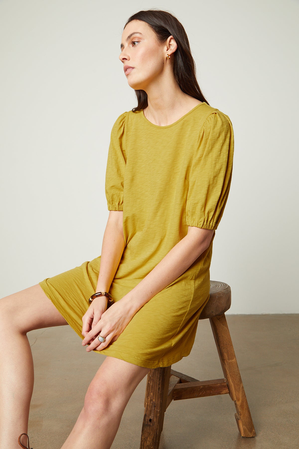 Model sitting on wooden stool wearing Meghan Dress in buttercup with puff sleeves front with hands in lap-26022635569345