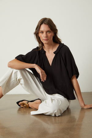 A woman is sitting on the floor in a Velvet by Graham & Spencer Ilene Puff Sleeve Top, with a V-neckline.