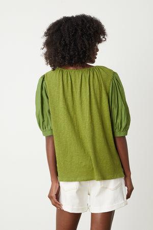 Woman sitting on stool in studio wearing Mallory Top in moss green with puff sleeves paired with white denim shorts back