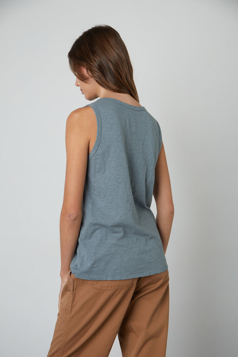 Person standing against a plain backdrop, shown from the back. They are wearing a Velvet by Graham & Spencer timeless crew neck sleeveless TAURUS TANK TOP and brown pants.