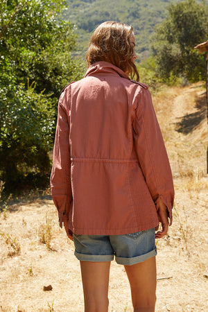 A woman in shorts and a RUBY LIGHT-WEIGHT ARMY JACKET by Velvet by Graham & Spencer is standing in a dirt field.