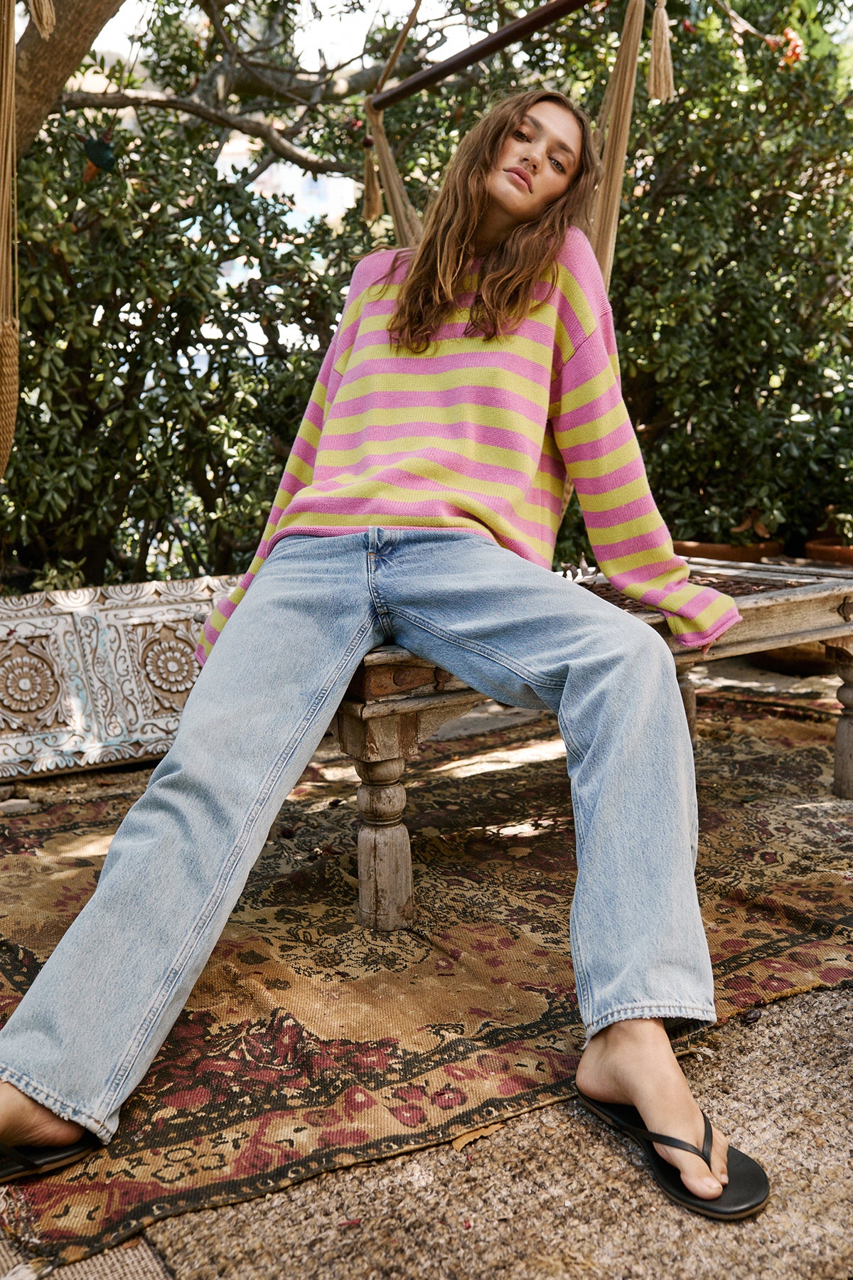 A woman sitting on a hammock wearing a Velvet by Graham & Spencer LEX STRIPED CREW NECK SWEATER and flip flops.-25954607235265