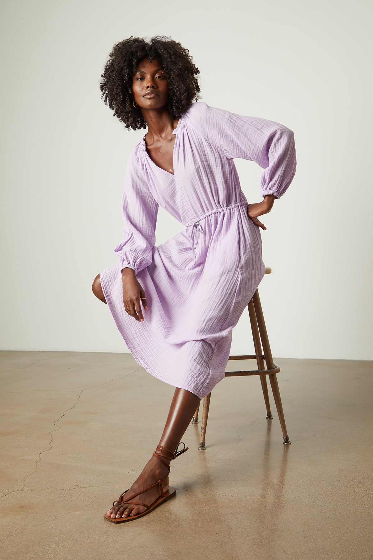 Model sitting on stool wearing Audrey cotton gauze dress in light lavender thistle color-26078934106305