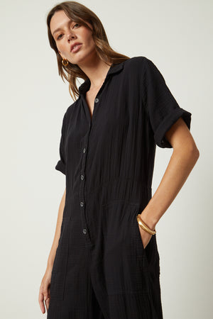 Elia jumpsuit in black with gold hoop earrings, bangle bracelet close up front woman hand in pocket