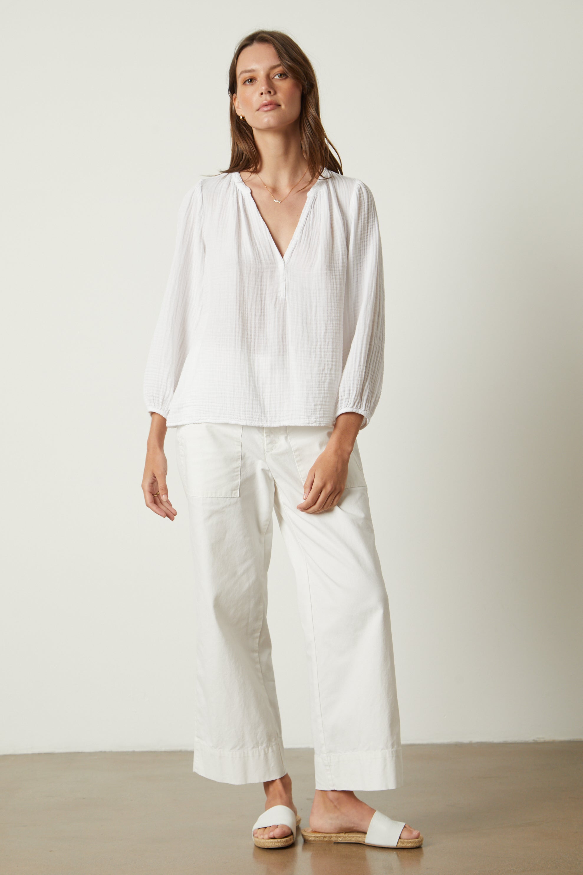   The model is wearing a white MAGGIE COTTON GAUZE V-NECK TOP blouse and white wide leg pants. (Brand Name: Velvet by Graham & Spencer) 