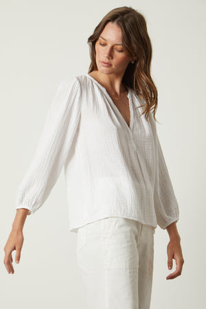 The model is wearing white pants and a Velvet by Graham & Spencer MAGGIE COTTON GAUZE V-NECK TOP.
