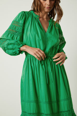 A woman is wearing a green Chanelle Cotton Lace Dress by Velvet by Graham & Spencer.