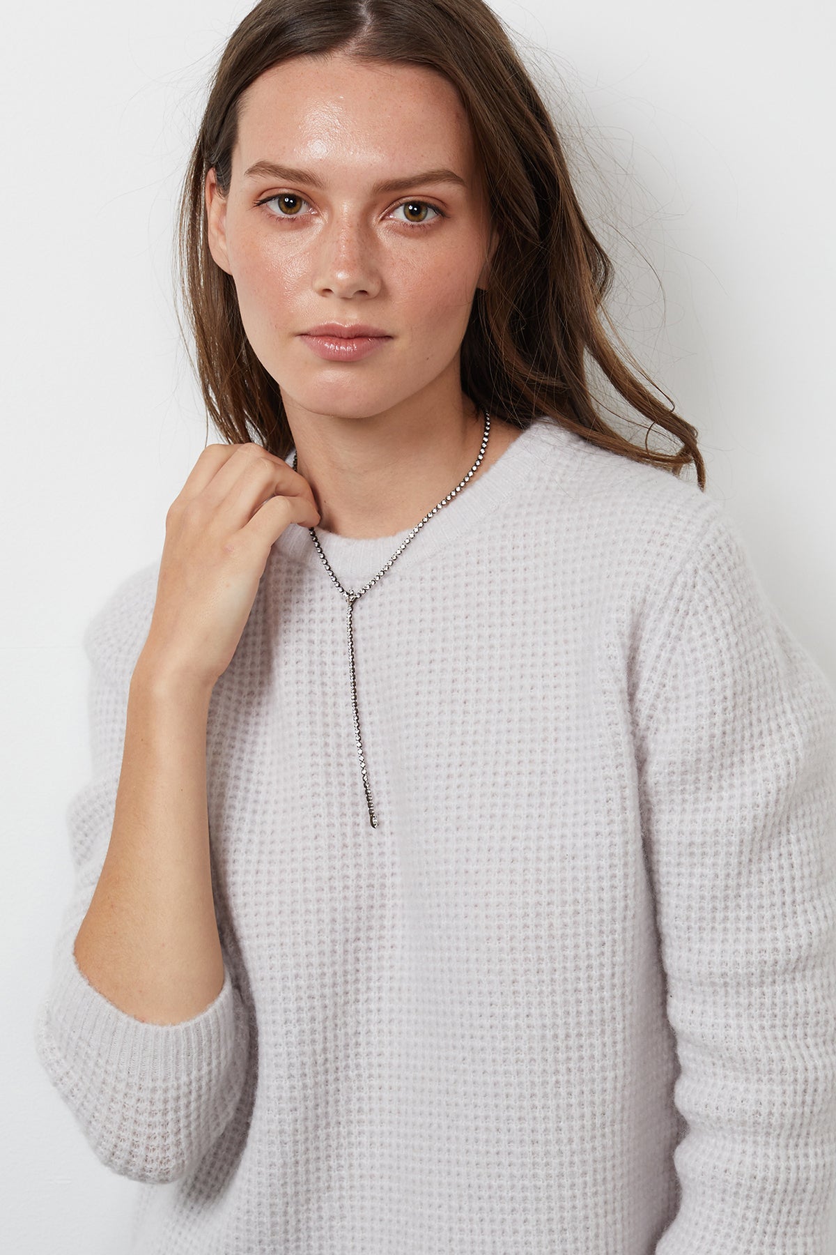   A woman with long hair is wearing the NADIE HONEYCOMB SWEATER, a light-colored wool blend piece by Velvet by Graham & Spencer, along with a pendant necklace. She stands against a plain white background, looking directly at the camera. 