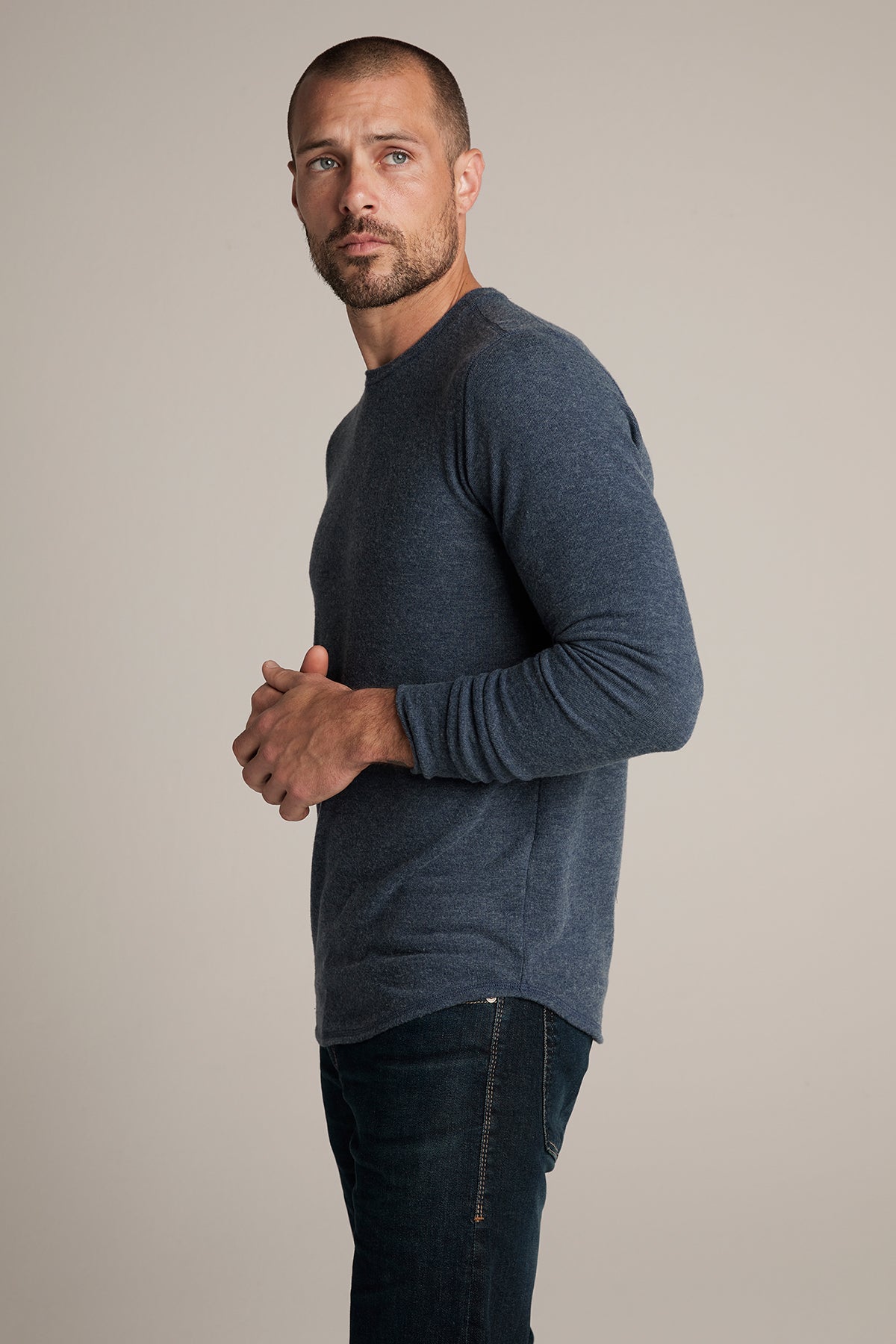   A man with a beard and short hair is wearing the BRONSON COZY JERSEY KNIT TOP by Velvet by Graham & Spencer and dark jeans. He is standing against a plain background, slightly turned to his left, looking forward. 