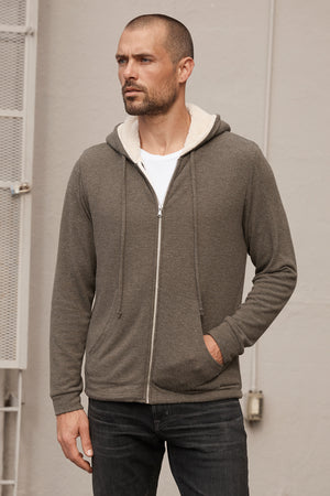 A man wearing a Velvet by Graham & Spencer SALVADORE SHERPA LINED HOODIE and jeans with an adjustable drawstring hood.