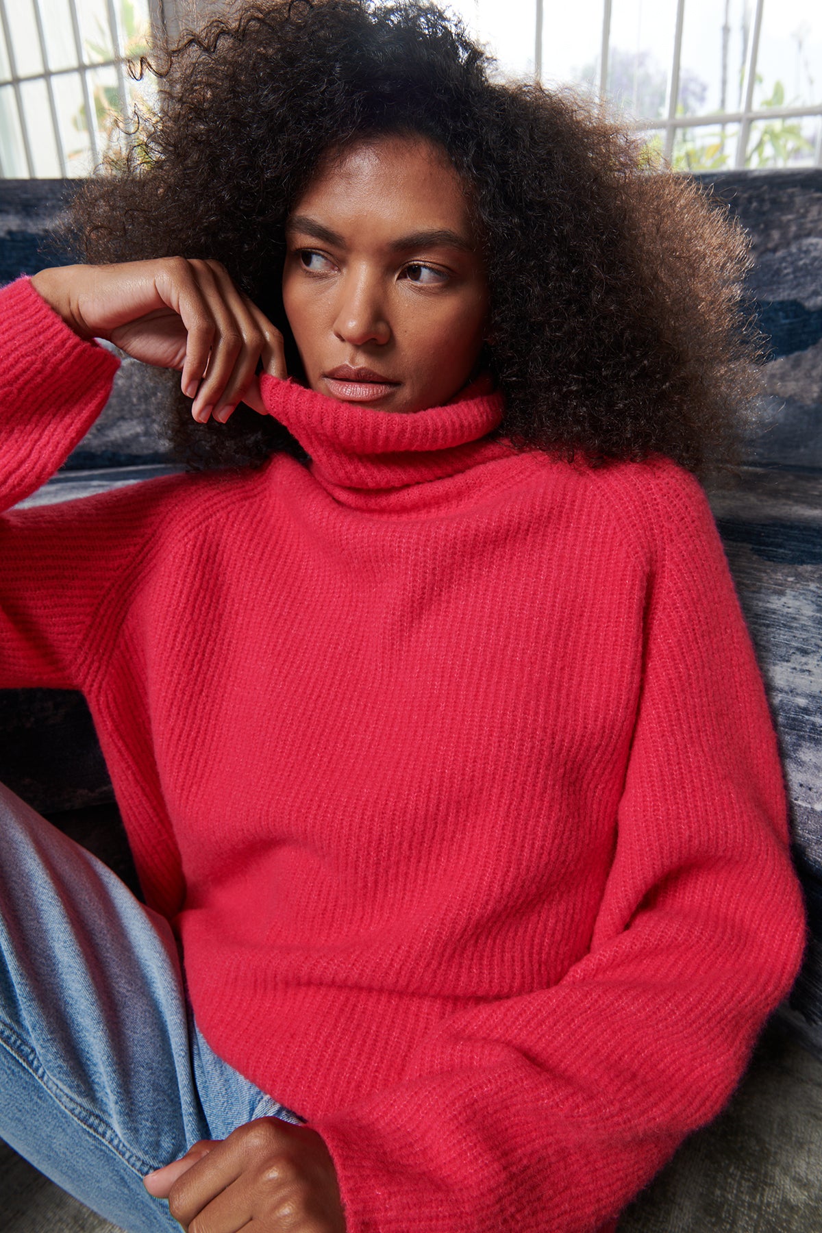   A woman is sitting on a couch wearing a red Velvet by Graham & Spencer Judith turtleneck sweater. 