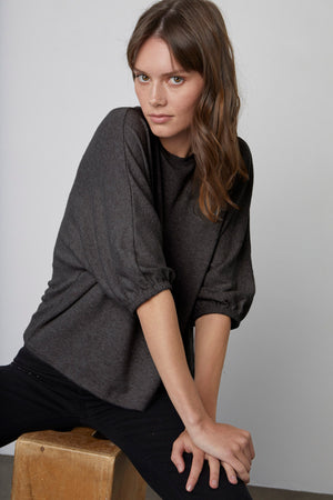 Model sitting on wooden crate wearing Makayla Crew Neck Pullover in anthracite and black denim Kate