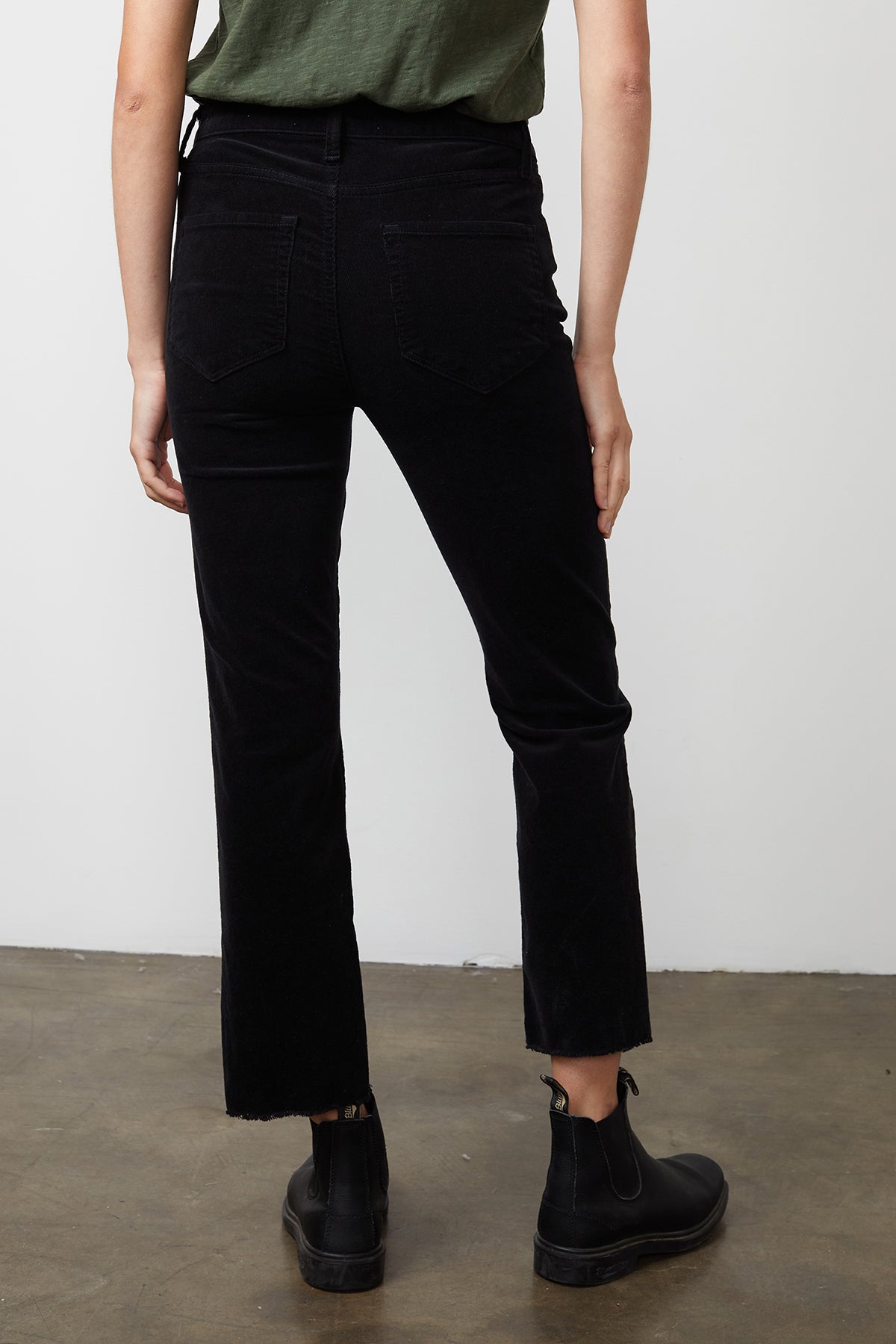   The back view of a person wearing Velvet by Graham & Spencer's CANDACE CORDUROY HIGH RISE CROP JEANS in a fall-inspired color scheme, with cropped cuffs. 