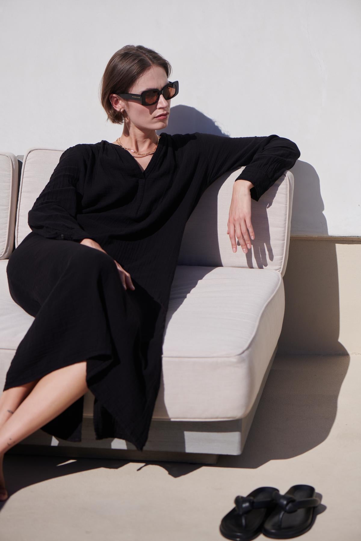 a woman sitting on a couch wearing sunglasses and a DOHENY DRESS by Velvet by Jenny Graham.-26293207335105