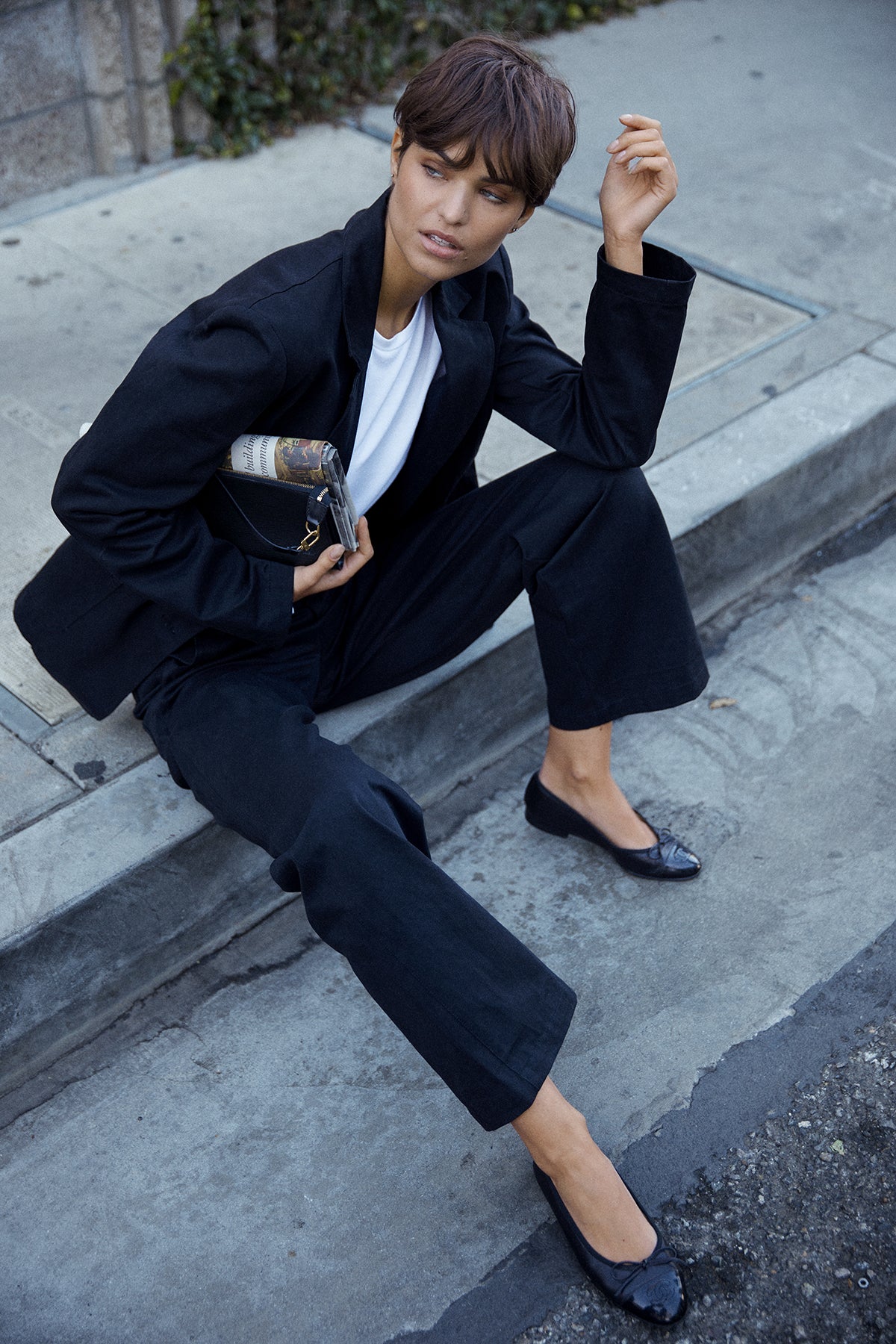   Model sitting on curb wearing Oversized Echo Blazer in Vintage Black with Long Sleeve Pacifica Tee in White and Ventura Pant 