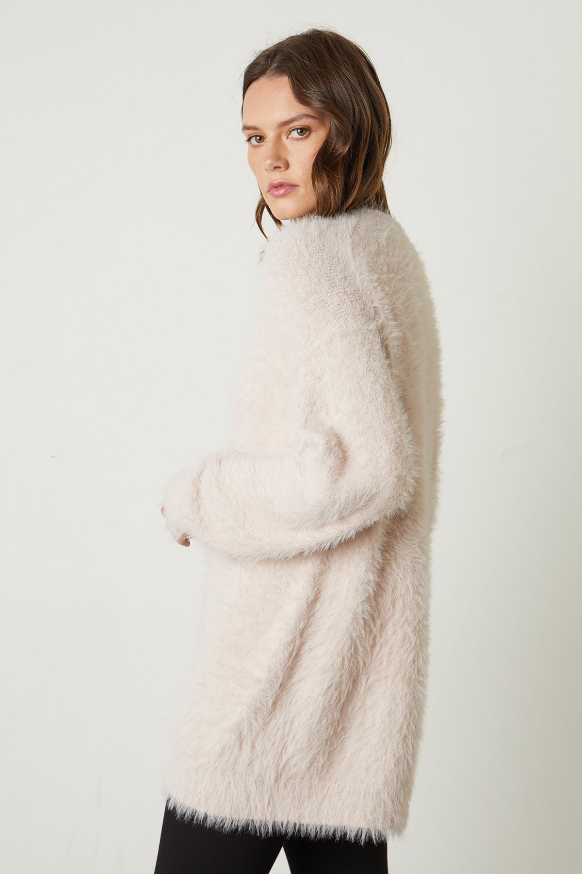   Model looking over shoulder wearing Barb Feather Yarn Button Front Cardigan in pale blush pink side & back 