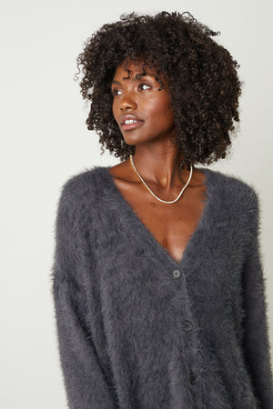 The model is wearing a Velvet by Graham & Spencer BARB FEATHER YARN BUTTON FRONT CARDIGAN.