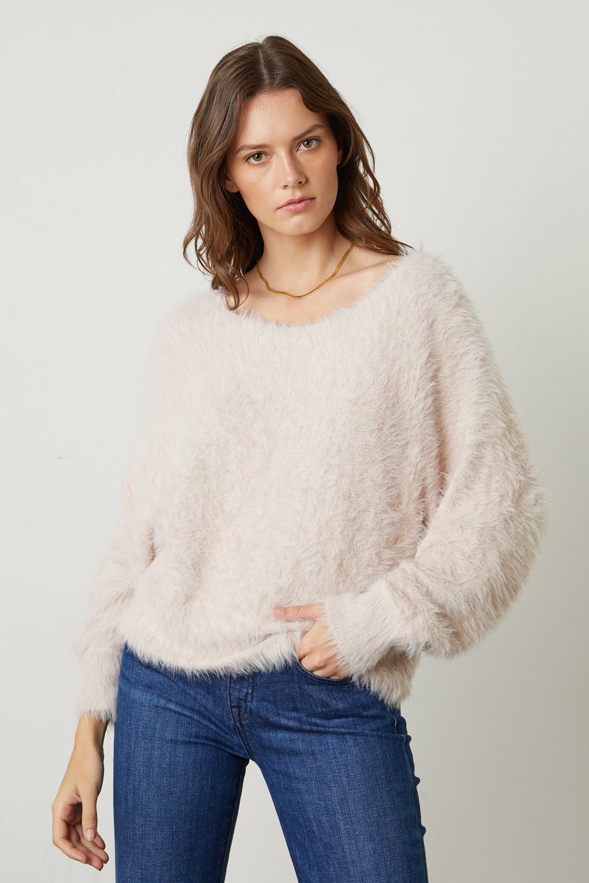 Model standing with hand in blue denim pocket wearing Betty Feather Yarn Boat Neck Sweater in pale blush pink front-25548650905793