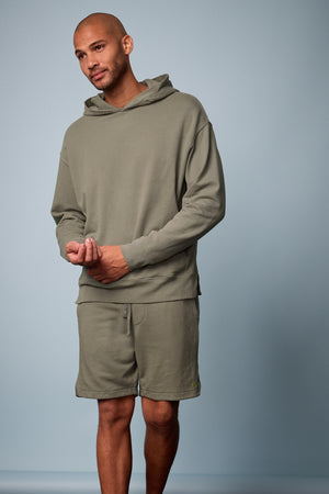 Lookbook image of Kane short in camp muted green french terry with Dan Hoodie, blue background, front