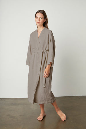 A woman wearing a Jenny Graham Home COTTON GAUZE ROBE standing in front of a white wall.