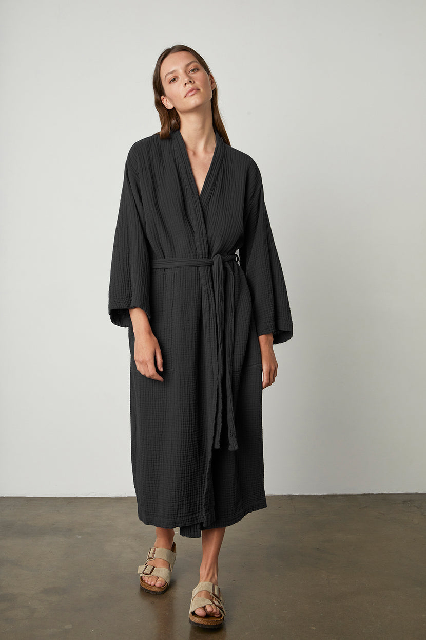 A woman wearing a black Cotton Gauze Robe by Jenny Graham Home and sandals.