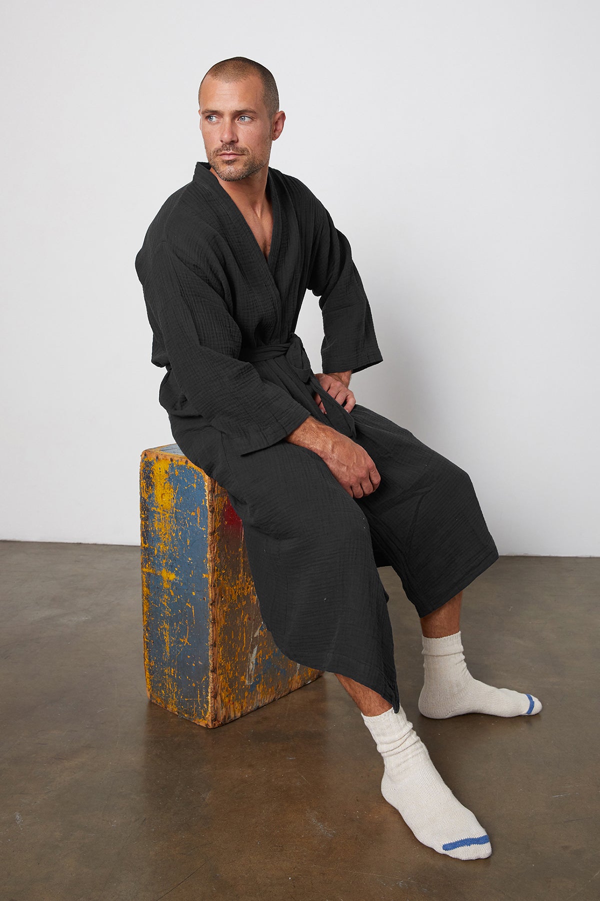   a man in a Jenny Graham Home Cotton Gauze Robe sitting on a wooden box. 