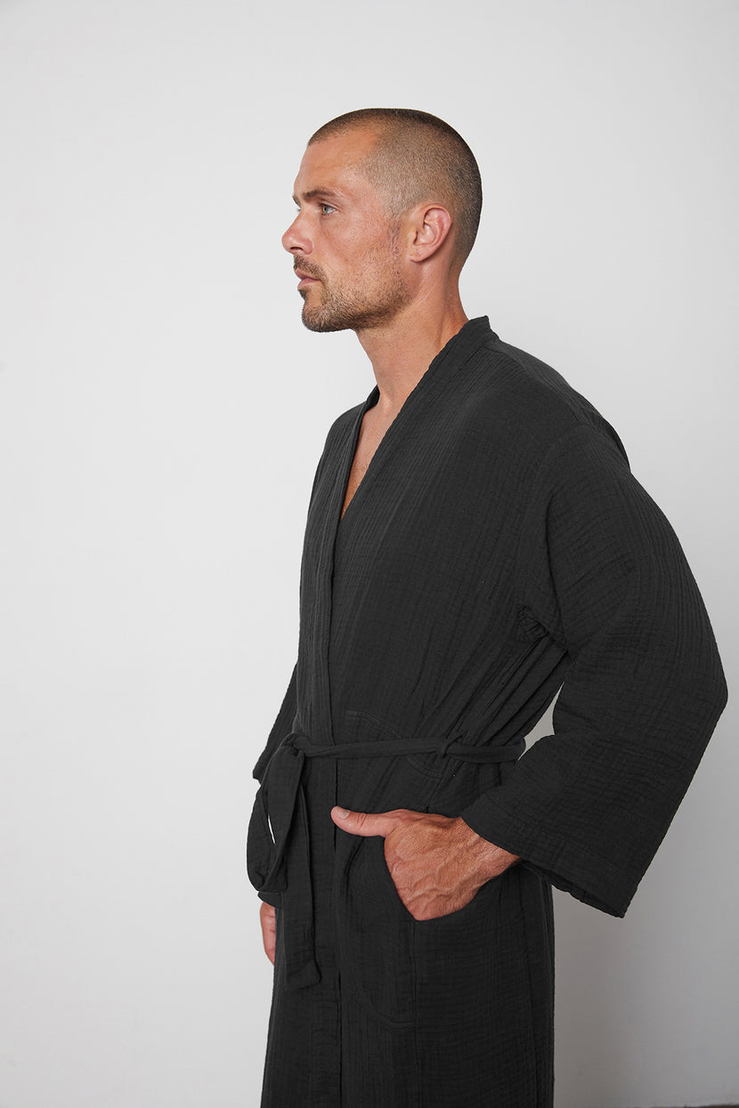a man in a black Jenny Graham Home Cotton Gauze Robe standing in front of a white wall.