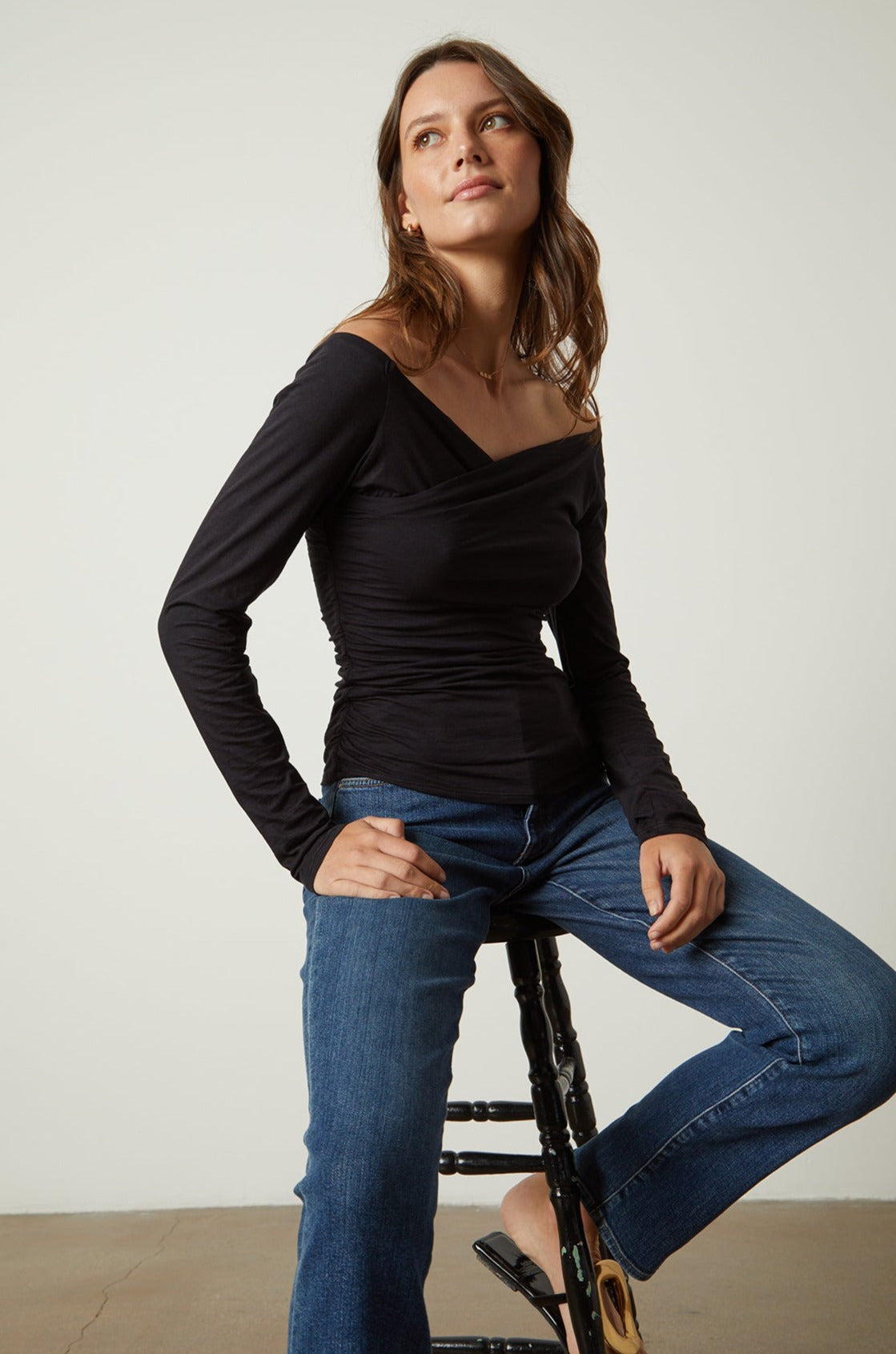   Model sitting on stool wearing Tabbie Shirred Fitted Tee in black with blue denim 