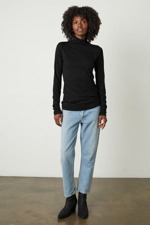 Talisia Gauzy Whisper Fitted Mock Neck Tee in black with light blue denim and black boots full length front